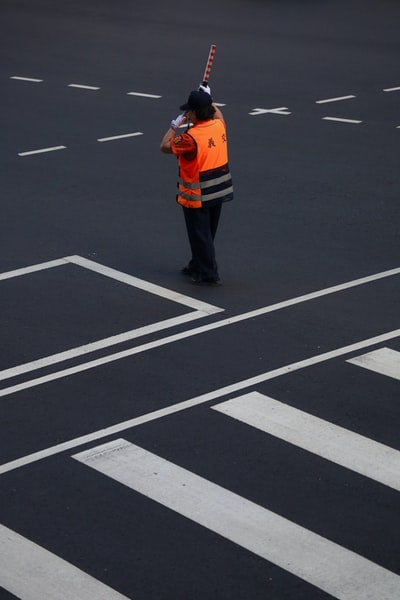 身穿橙色夹克和黑色裤子的男子站在黑白相间的行人线上